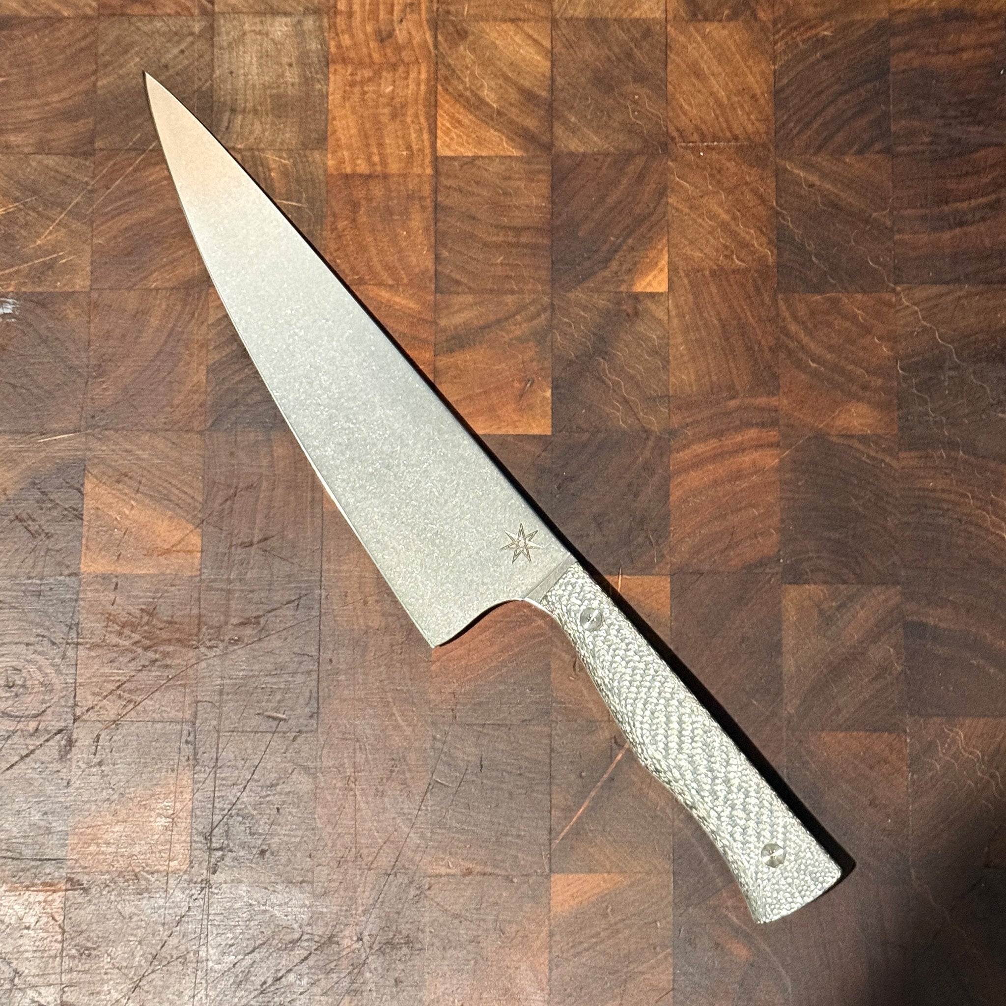 Chef Knife with a textured silver carbon fiber handle on a wooden surface